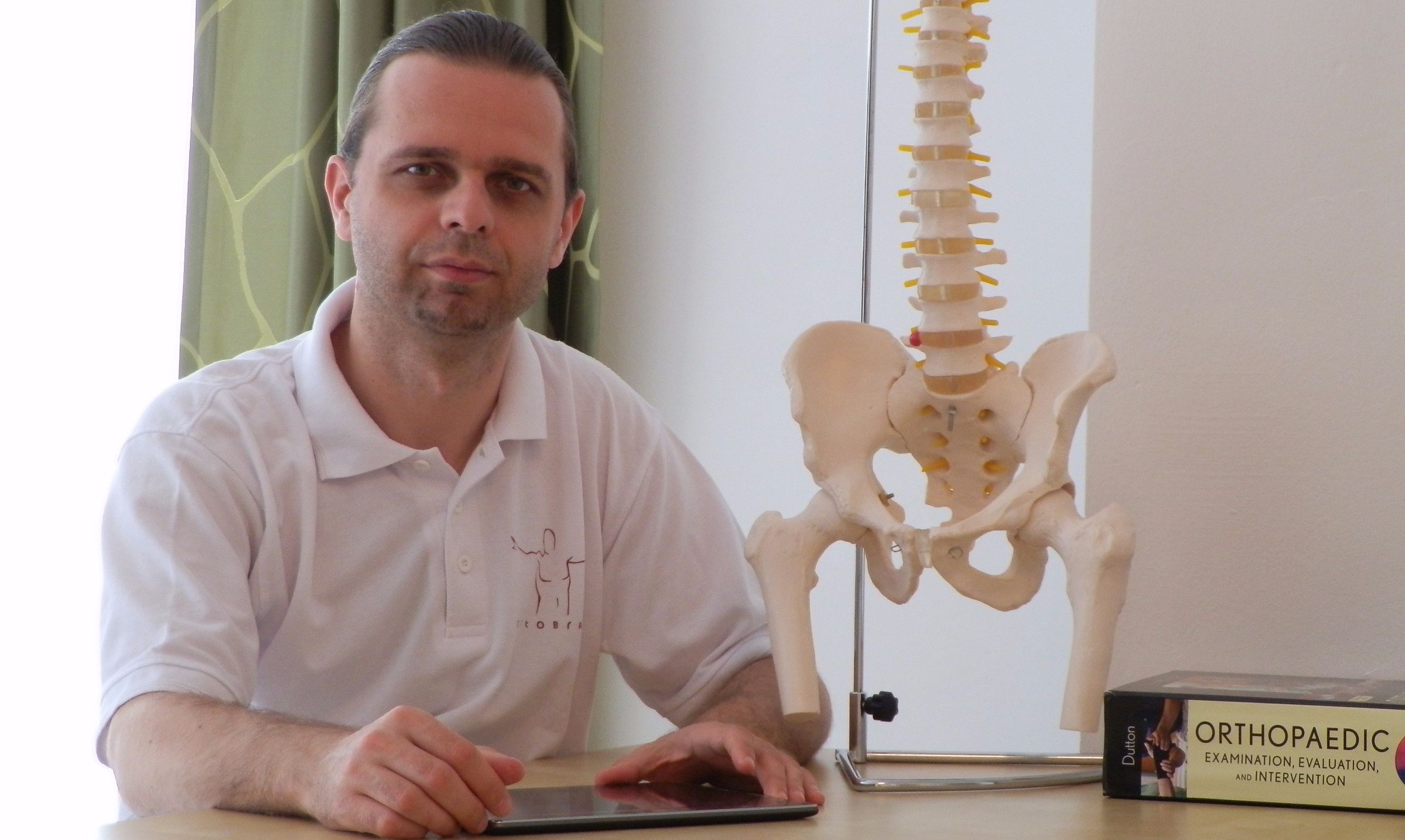 Dr. László Gábos sitzt neben einem Becken- und WIrbelsäulenmodell