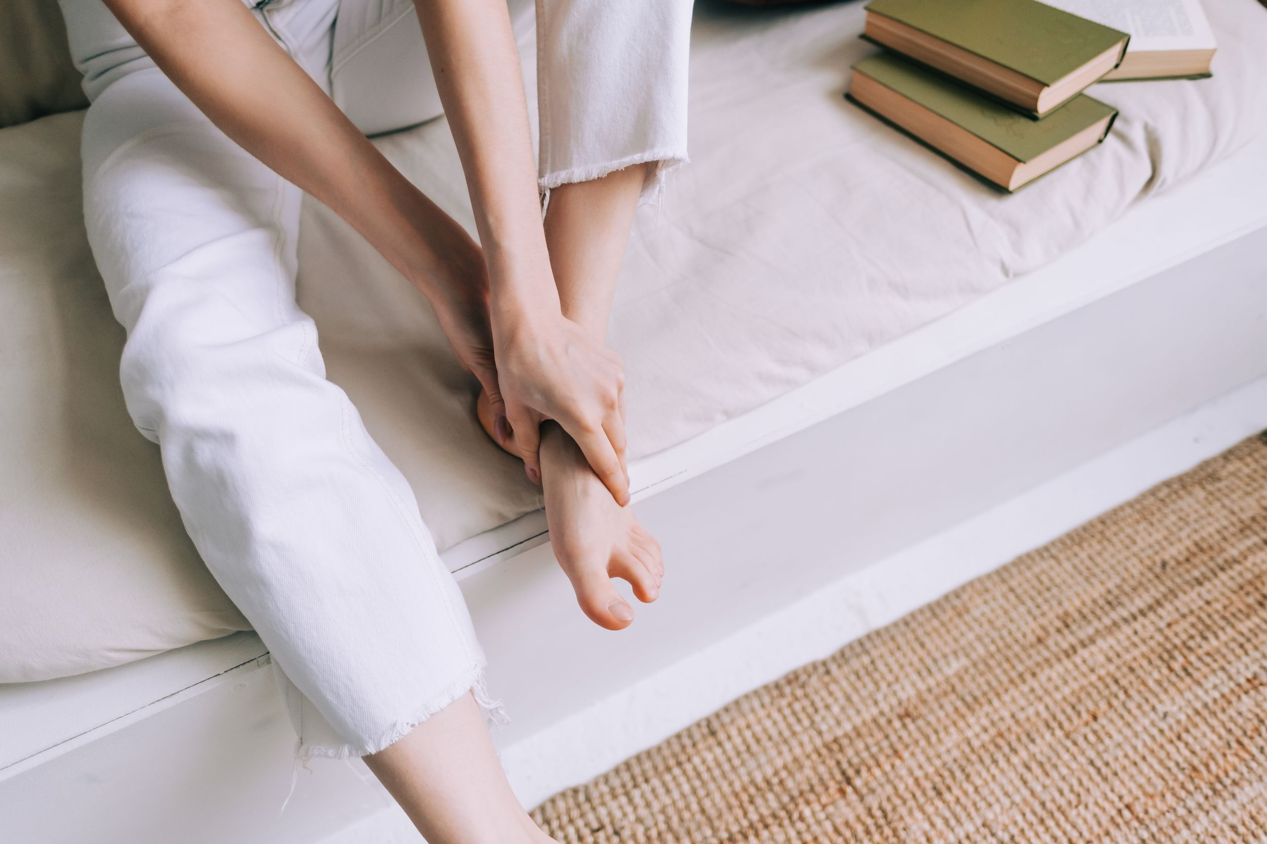 Eine Frau sitzt auf einem Bett und hält sich den Fuß